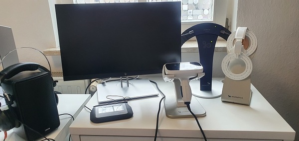 Auf einem Schreibtisch stehen ein Monitor, medizinische Geräte und Kopfhörer für Hautanalyse.